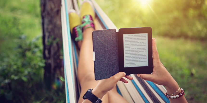 Une femme, dans un hamac, lisant un livre sur son Kindle, concentrée et détendue dans un cadre extérieur confortable.