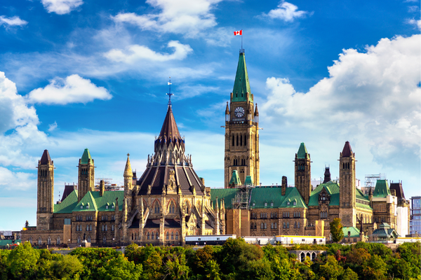 Les édifices du Parlement canadien à Ottawa, avec leurs toits en cuivre vert, leur architecture gothique et leur haute tour centrale surmontée du drapeau canadien.